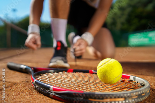Tennis player tying his shoes. Selective focus on the ball and racket © Andrii 