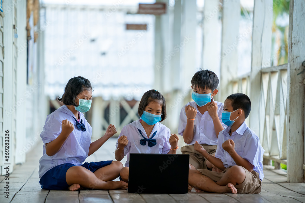 Group of students wearing protective mask to Protect Against Covid-19 use laptop to have online class happily at Thailand school classroom. Group of students wearing protective mask to Protect Against Covid-19 use laptop to have online class happily at Thailand school classroom.
