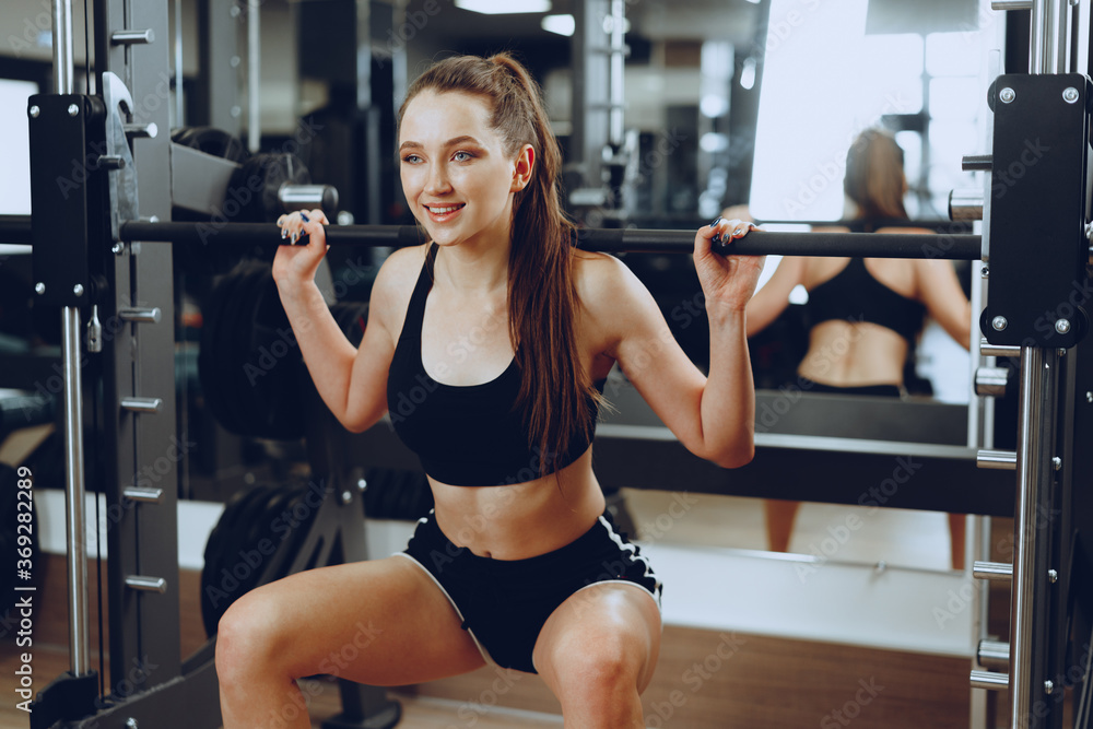 Young woman doing squats with barbell in a gym apparatus Young woman doing squats with barbell in a gym apparatus