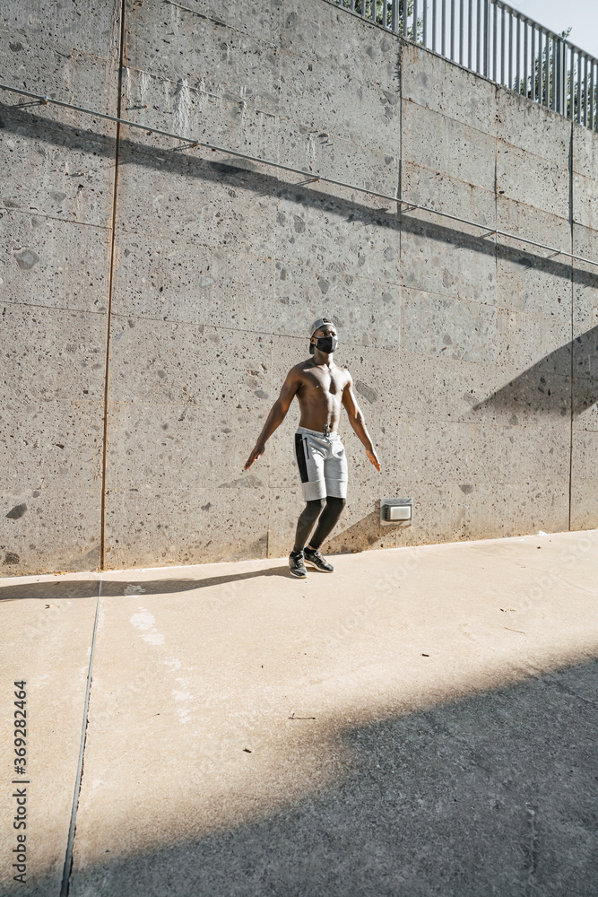 Athletic black man is training in urban area while wearing a mask. Athletic black man is training in urban area while wearing a mask.