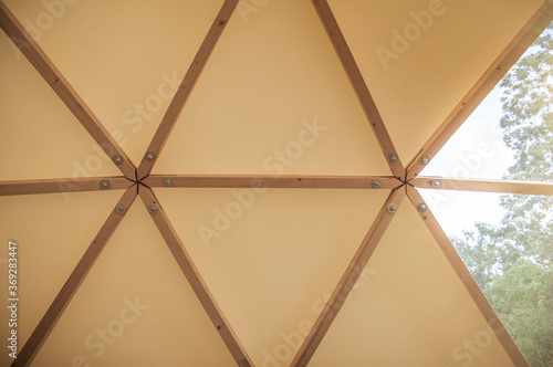 Interior of large geodesic wooden dome tent construction detail with window and view to forest. Empty interior glamping tent.