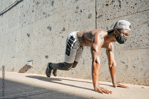 Athletic black man is training in urban area while wearing a mask.