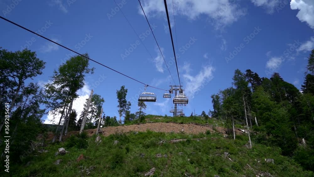 Close-up in the open air, mountain lifts are moving in different directions, people are sitting on them. Against the background of beautiful nature, the sky with clouds, mountains and trees Close-up in the open air, mountain lifts are moving in different directions, people are sitting on them. Against the background of beautiful nature, the sky with clouds, mountains and trees