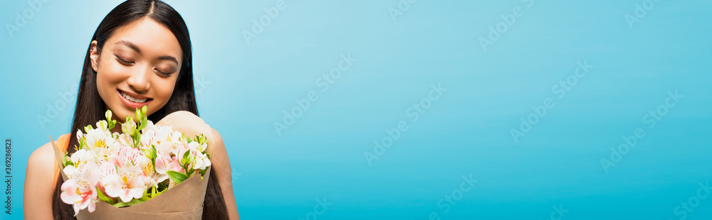 panoramic crop of happy asian girl smiling and holding flowers on blue panoramic crop of happy asian girl smiling and holding flowers on blue