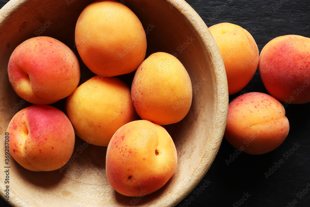 Photography of apricots in a wooden bowl, on slate background for food illustrations Photography of apricots in a wooden bowl, on slate background for food illustrations