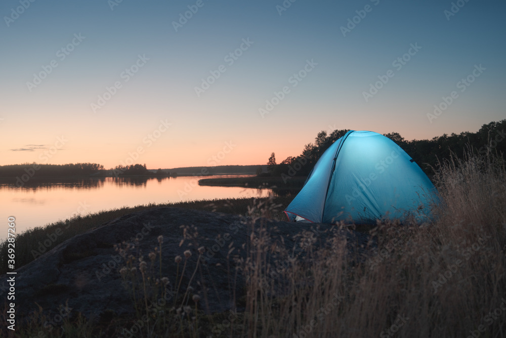 Glowing tent on the shores of a picturesque lake during the white nights.