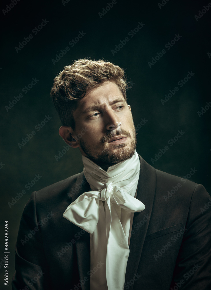 Sincere sin. Young man in suit as Dorian Gray isolated on dark green background. Retro style, comparison of eras concept. Beautiful male model like classic literature character, old-fashioned. Sincere sin. Young man in suit as Dorian Gray isolated on dark green background. Retro style, comparison of eras concept. Beautiful male model like classic literature character, old-fashioned.