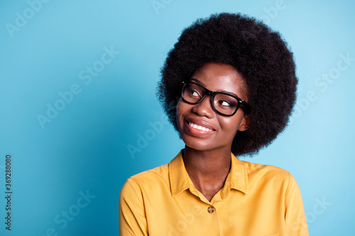 Photo of dark skin extensive hairstyle woman beaming toothy smiling dreamy inspired look copyspace fantasy about spirit world wear eyeglasses yellow shirt isolated blue color background