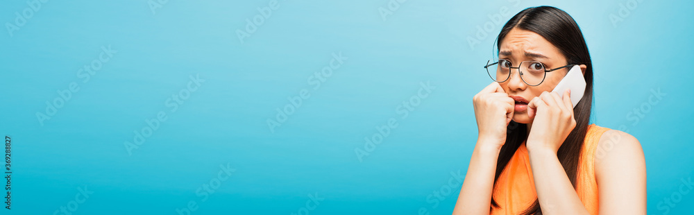 panoramic concept of stressed asian girl in glasses talking on smartphone isolated on blue panoramic concept of stressed asian girl in glasses talking on smartphone isolated on blue
