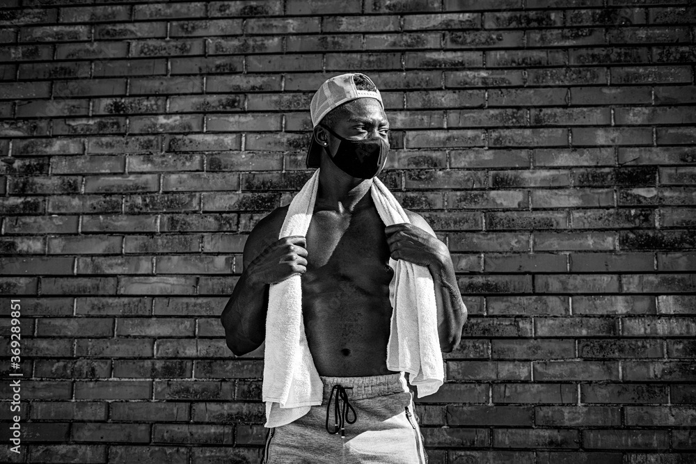 Athletic black man is training in front of the grey wall while wearing a mask. Black and white photo. Athletic black man is training in front of the grey wall while wearing a mask. Black and white photo.