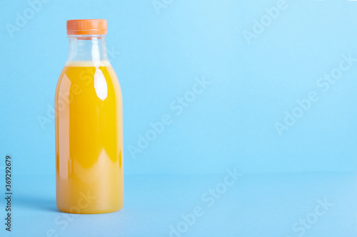 Freshly squeezed orange juice in bottle on blue background. 