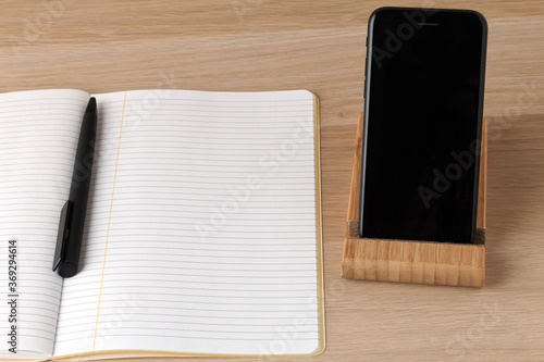 a empty lined pages of notebook opened with black pen in the middle lying, a black phone on a stand with a black screen, minimalistic clean working place, space to make plans, write down new ideas