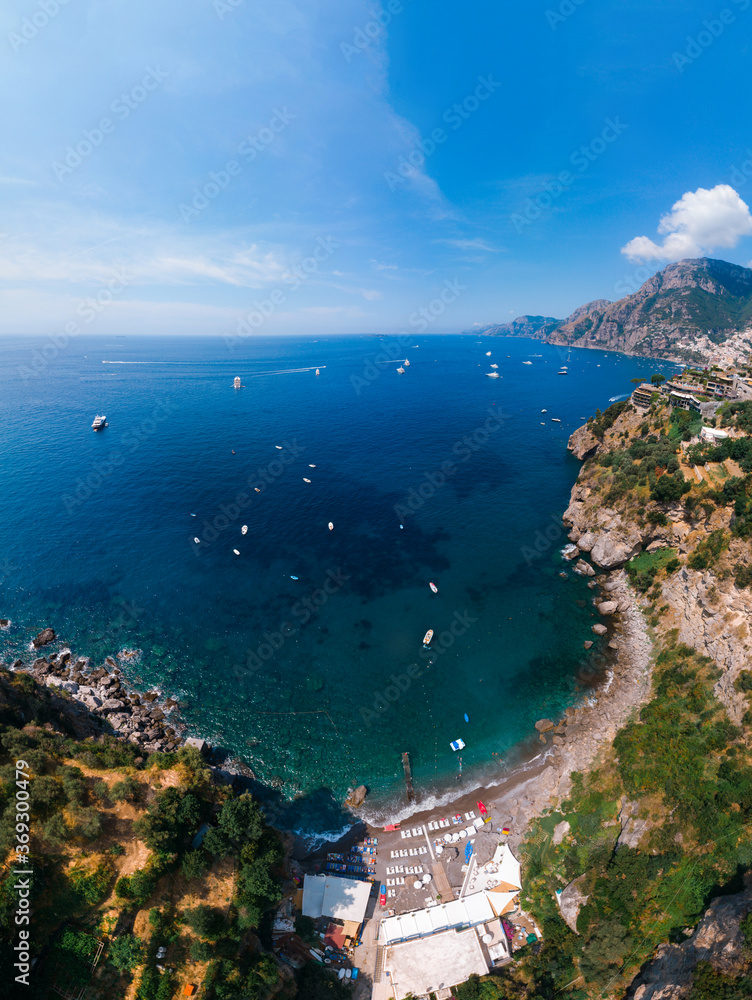 Aerial view of Laurito little cliff beach, Positano - popular tourist destination in Italy. Sunny summer day. vertical photo, clear sea and green mountains of Sorrento. Travel and vacation.