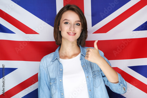Beautiful young woman standing and showing thumb up on british flag background