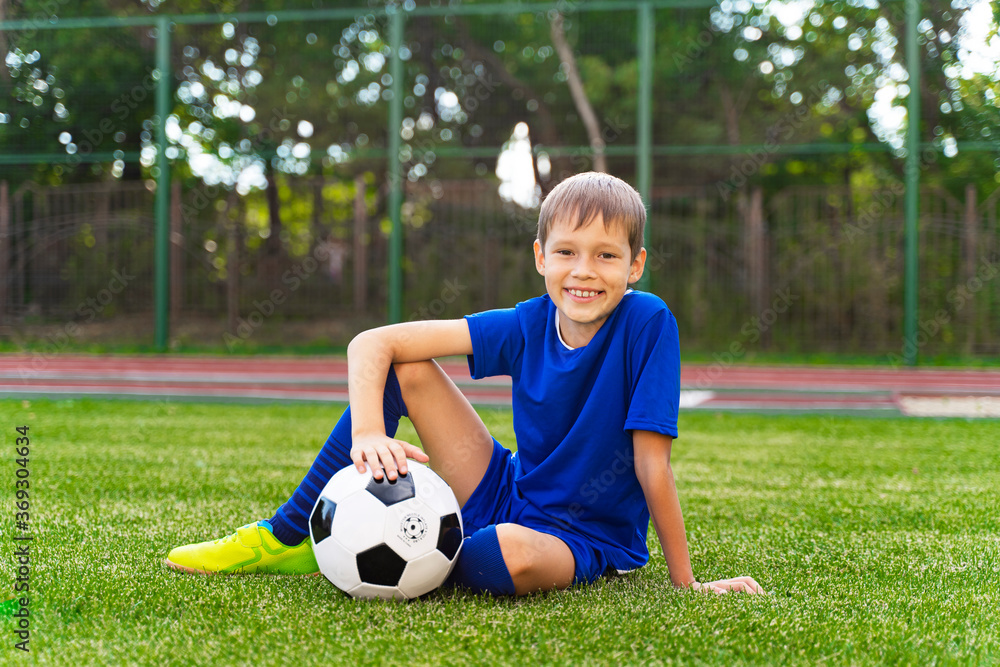 A little boy sits on a green soccer field, a soccer ball A little boy sits on a green soccer field, a soccer ball