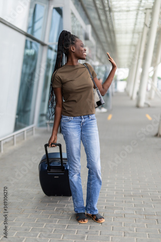Young african woman wave hello gretting while carry baggage in airport terminal outdoors