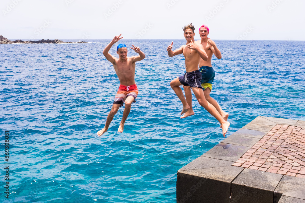 group of friends jumping off together at the beach doing flips and having fun in the water - people enjoyinng thei holiday at the beach playing and laughing - looking at the camera while jumping