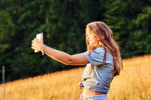 Young girl taking selfie outdoors in summer at sunset 