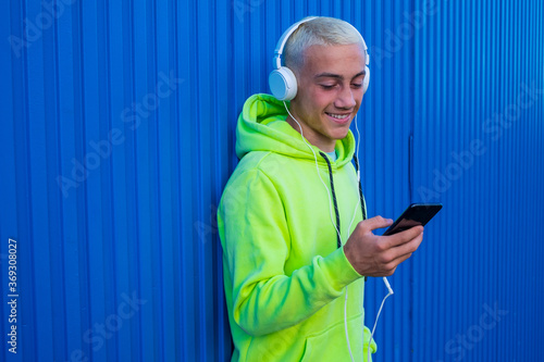 one teenager using his phone smiling and having fun looking at it while hearing music with white headphones  photo