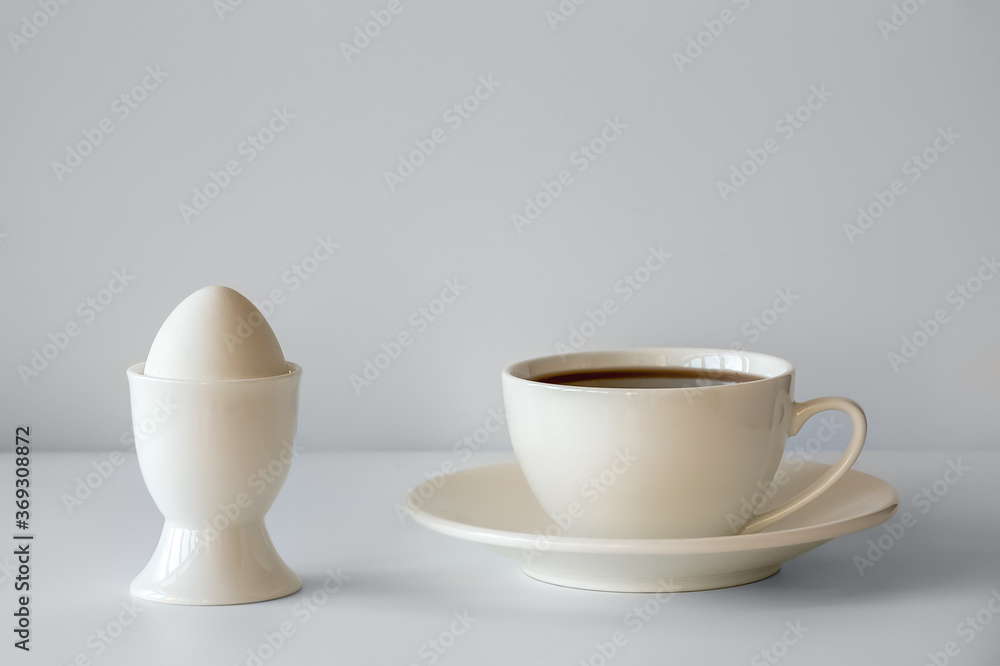 Boiled egg in an egg Cup and tea in a white Cup. White dishes on a white background. Breakfast consists of a boiled egg and a Cup of tea. Boiled egg in an egg Cup and tea in a white Cup. White dishes on a white background. Breakfast consists of a boiled egg and a Cup of tea.