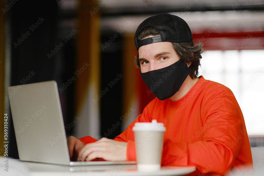 The man sits alone at a table in the open space, drinking coffee and working on his laptop. Freelance concept The man sits alone at a table in the open space, drinking coffee and working on his laptop. Freelance concept