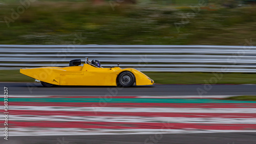 A panning shot of a yellow racing car as it circuits a track.