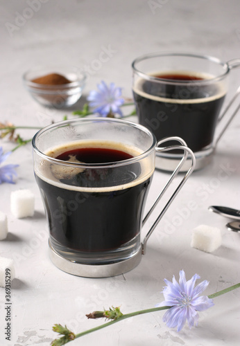 Chicory beverage in two glass cups, with concentrate and flowers on grey background. Healthy herbal beverage, coffee substitute, Closeup, Vertical format
