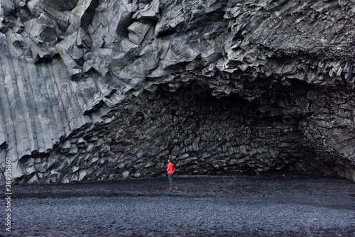 Iceland tourist woman walking on Reynisfjara black sand beach by basalt columns and cave, beach of Vik, South Iceland coast. Happy woman visiting tourist attraction destination. photo