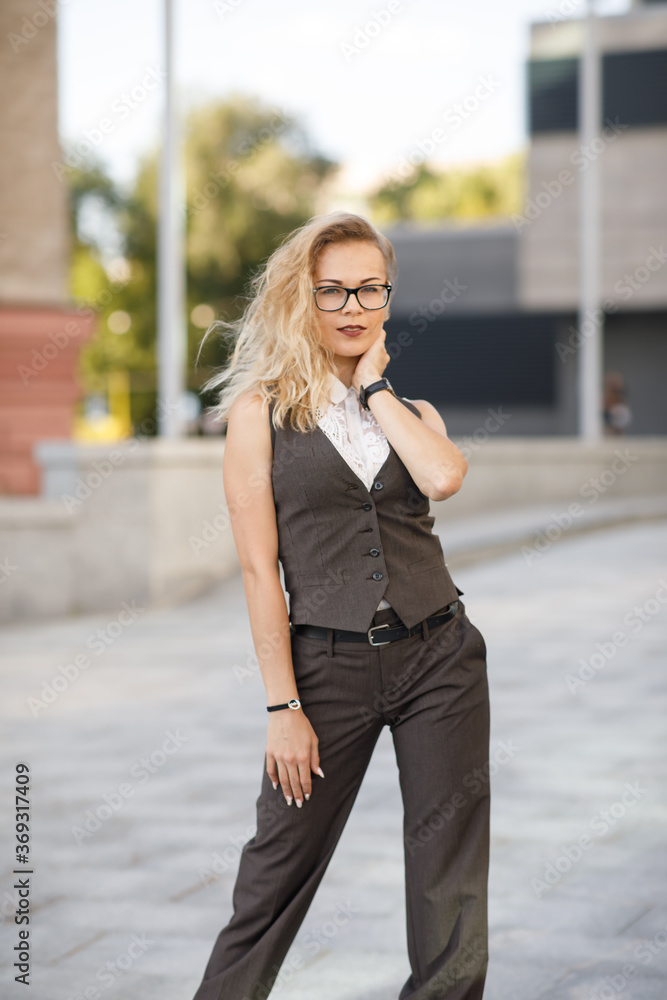 Beautiful young business woman with blond curly hair wearing a suit  and glasses poses outdoors