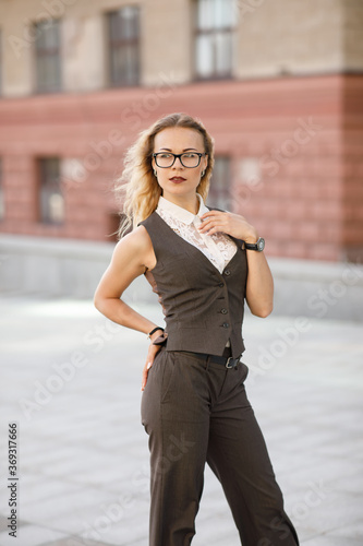 Beautiful young business woman with blond curly hair wearing a suit  and glasses poses outdoors © Dmitry