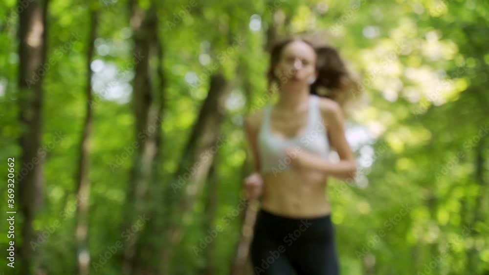 An exhausted tired young woman with earphones is running in park An exhausted tired young woman with earphones is running in park