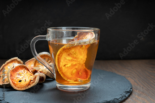 Thai traditional healing matoom tea made of dried bael fruit slices, also known as stone apple, in transparent glass cup on stony tray on dark wooden table. Image with selective focus and copy space