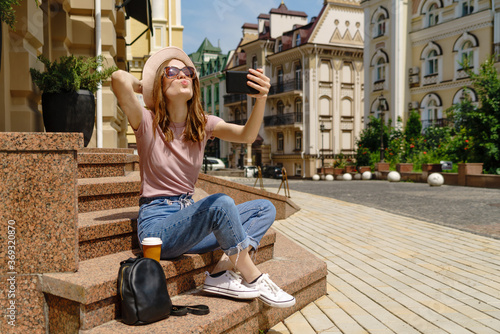 Beautiful Young Woman tourist with takeout coffee sitting on stairs using smartphone