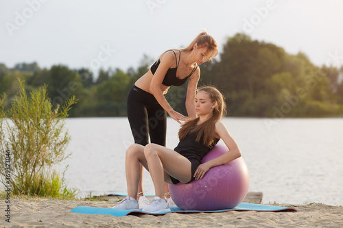 A fitness trainer shows a young girl how to do a proper exercise on a gym ball