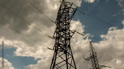 Wide view of clouds passing behind power line pylon in sunset sky background, time lapse
