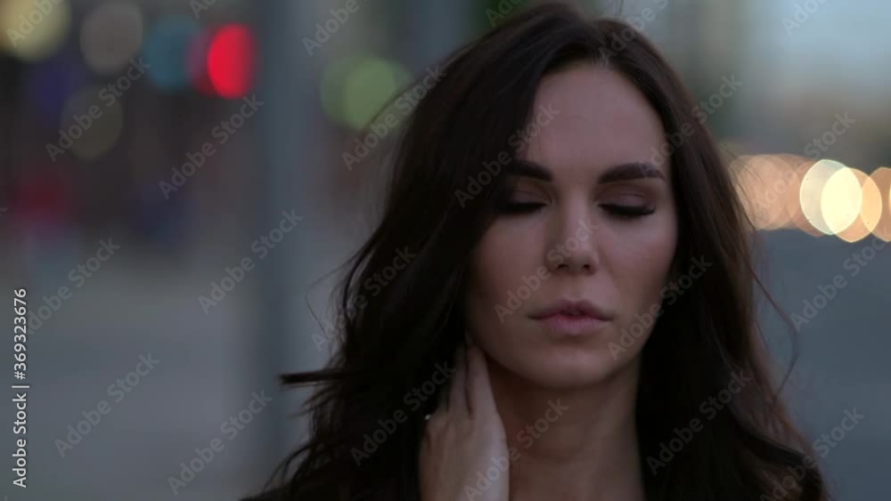 Close-up portrait of the face of a bright dark-haired girl, she is against the background of evening city lights, walking near the highways