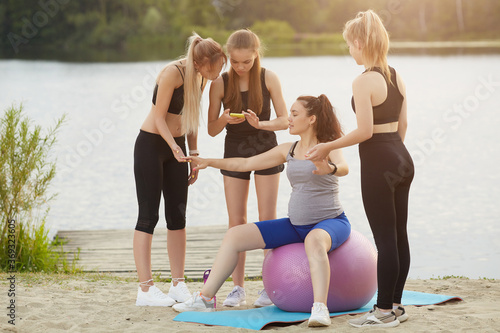 pregnant woman doing fitness exercises with a ball with a trainer and friends