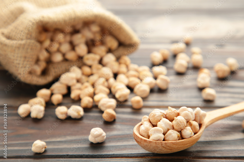 Uncooked chickpeas in wooden spoon and bag on brown background Uncooked chickpeas in wooden spoon and bag on brown background