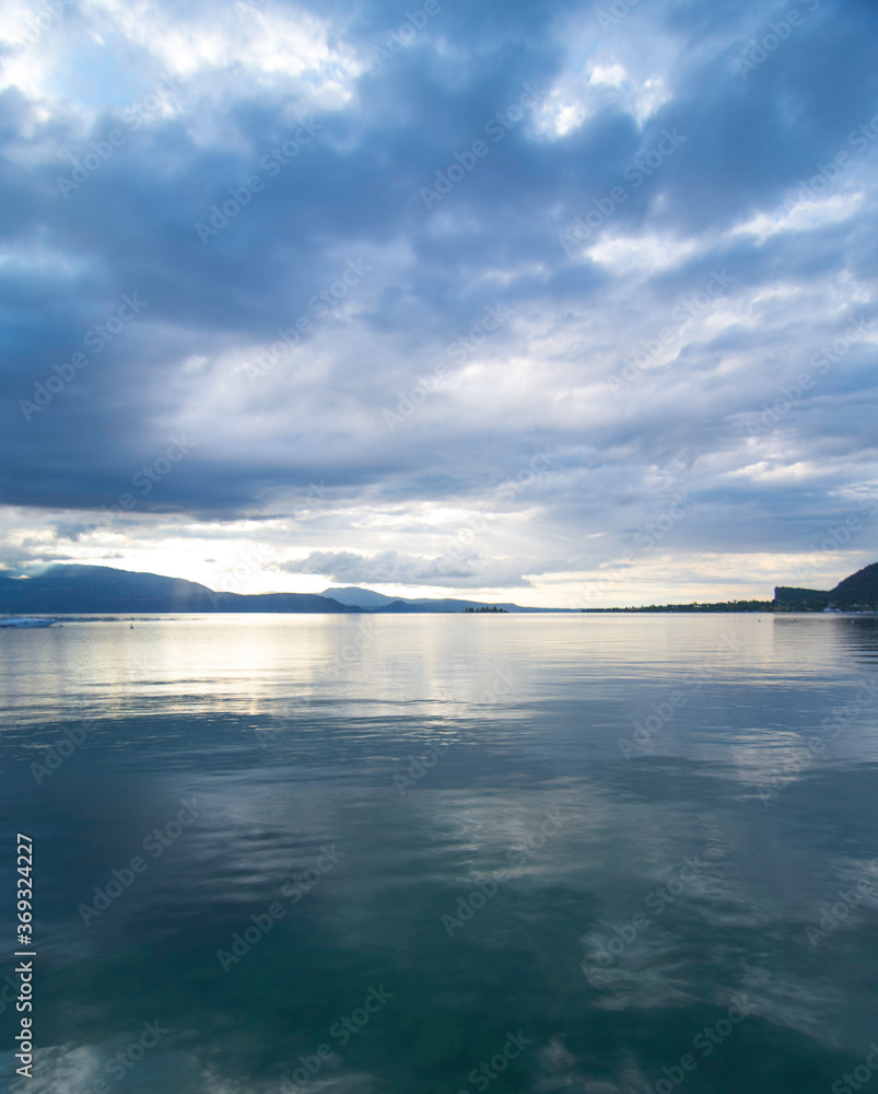 View of Lake Garda in the early morning or evening. The water is calm, the sky is partly cloudy. Small boats dance on the water. The mood is dreamy. morning Mood