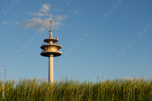 Big weather station against a blue sky with gray clouds, green barley field (Hordeum vulgare) is out of focus by motion, orange colors by evening sun. The main motif is on the left in the picture.