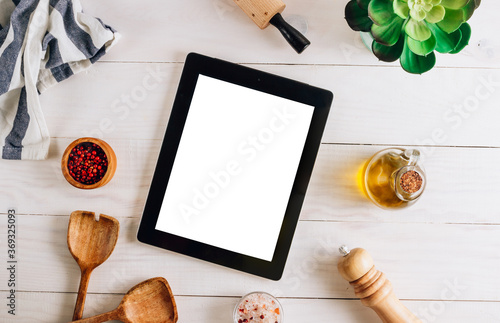 Tablet with blank screen and different kitchen and cooking utensils on whie wooden table. Culinary blog, recipe template, online cooking courses photo