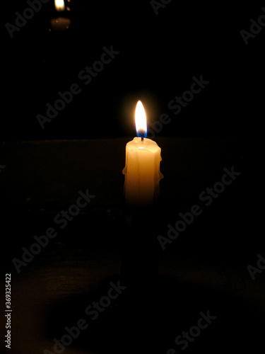 Flame of single burning wax candle close up on black background isolated. Religious atmosphere, sadness or romantical mood concept for your design. Light of candle in night as symbol of hope