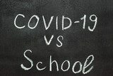 COVID-19 against school is written on a blackboard in white chalk.