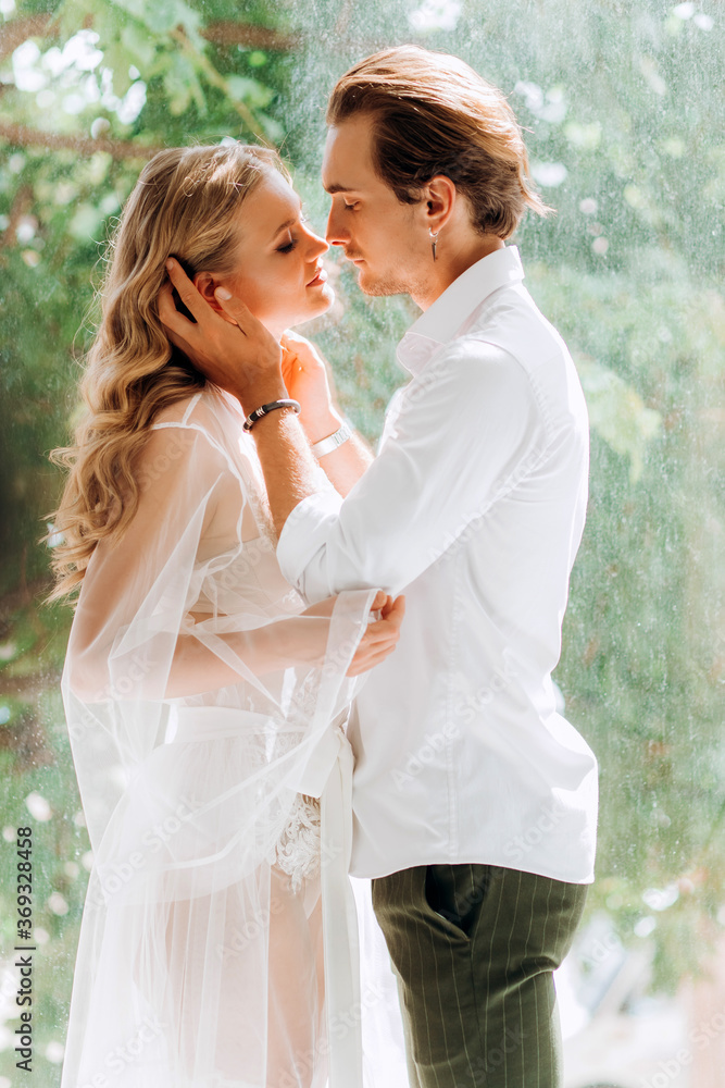 A beautiful bride and a young groom are standing near a window in a white studio. Wedding in the interior. Wedding portrait of newlyweds in love.
