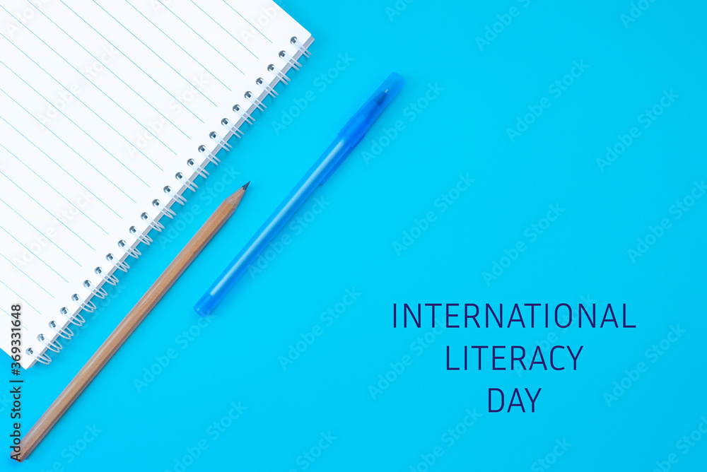 Notebook, pen and pencil on a blue background. The text of the international literacy day. Concept of education, September 1, Teacher's Day. Flat lay, copy space. Notebook, pen and pencil on a blue background. The text of the international literacy day. Concept of education, September 1, Teacher's Day. Flat lay, copy space.