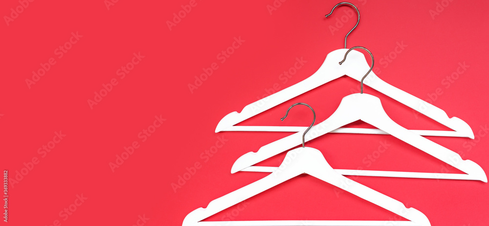 Three white wooden hangers on a red background. Banner for a blog about women's fashion. The concept of fashion, shopping, sales, black Friday. Flat lay, copy  space
