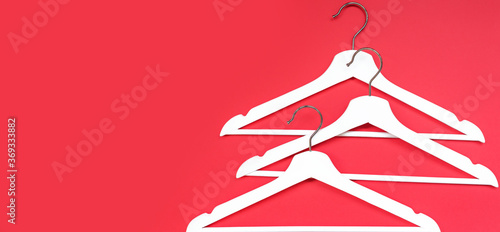 Three white wooden hangers on a red background. Banner for a blog about women's fashion. The concept of fashion, shopping, sales, black Friday. Flat lay, copy space