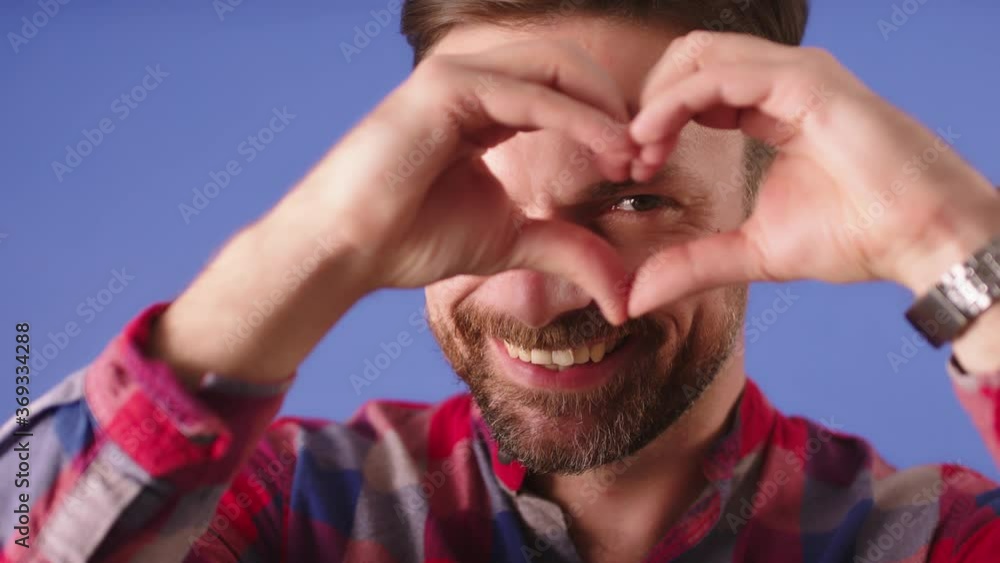 Young caucasian flirty bearded man with hand gesture heart over his eye. slow motion High quality 4k footage Young caucasian flirty bearded man with hand gesture heart over his eye. slow motion High quality 4k footage