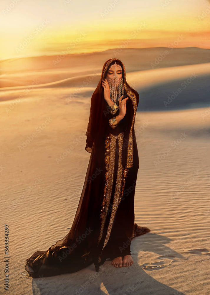 Beautiful mysterious arab woman in black muslim abaya dress. head is  twisted with silk handkerchief chain hides face. Fantasy Girl walks in  desert, art background sand golden sunset. Queen Concubine, obrazy,  fototapety,