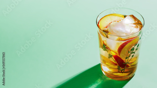 Sparkling cold brew peach tea with thyme in glass on green paper background close-up. Refreshing summer non-alcoholic drink concept photo